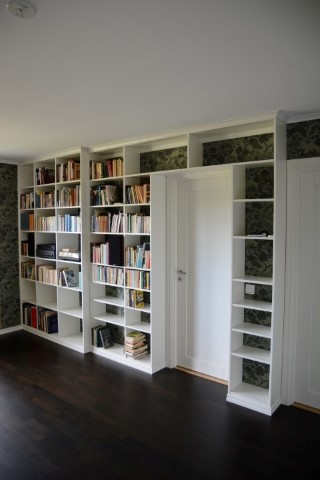 vit bokhylla med olika djup inbyggd runt dörröppning